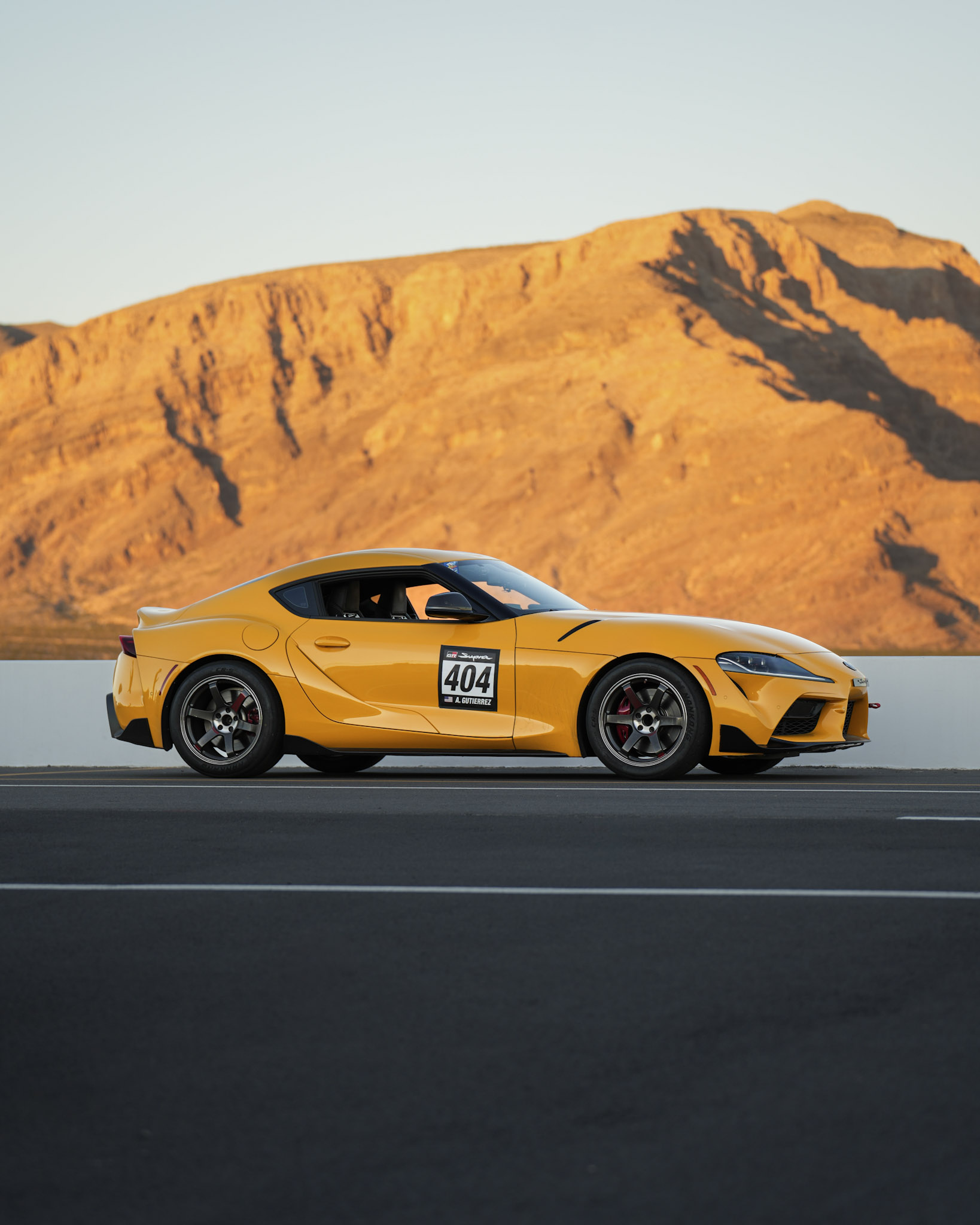 Yellow Toyota GR Supra #404 parked against golden mountain backdrop at Spring Mountain Raceway
