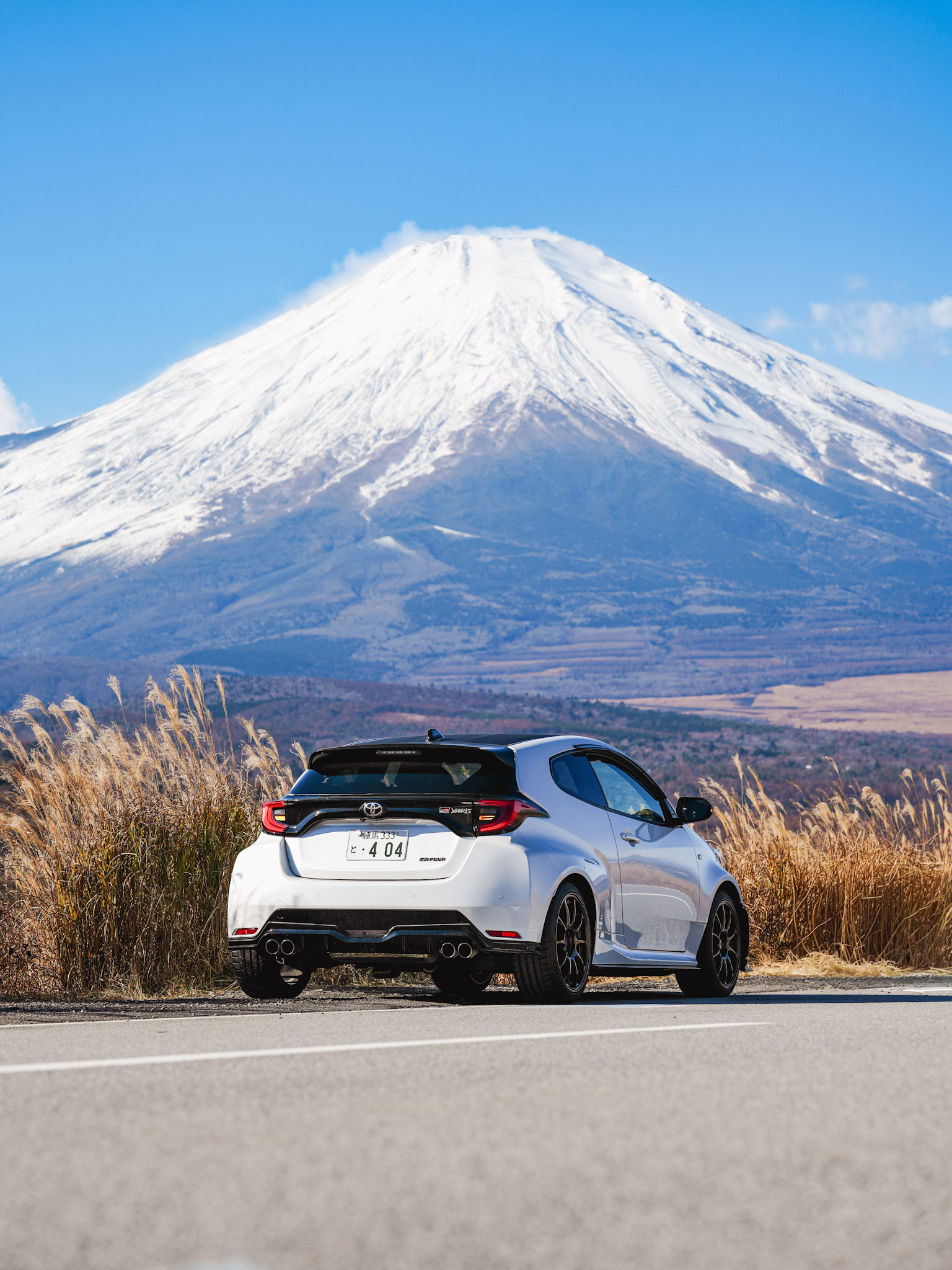 White Toyota GR Yaris rear with Mt. Fuji and silver pampas grass