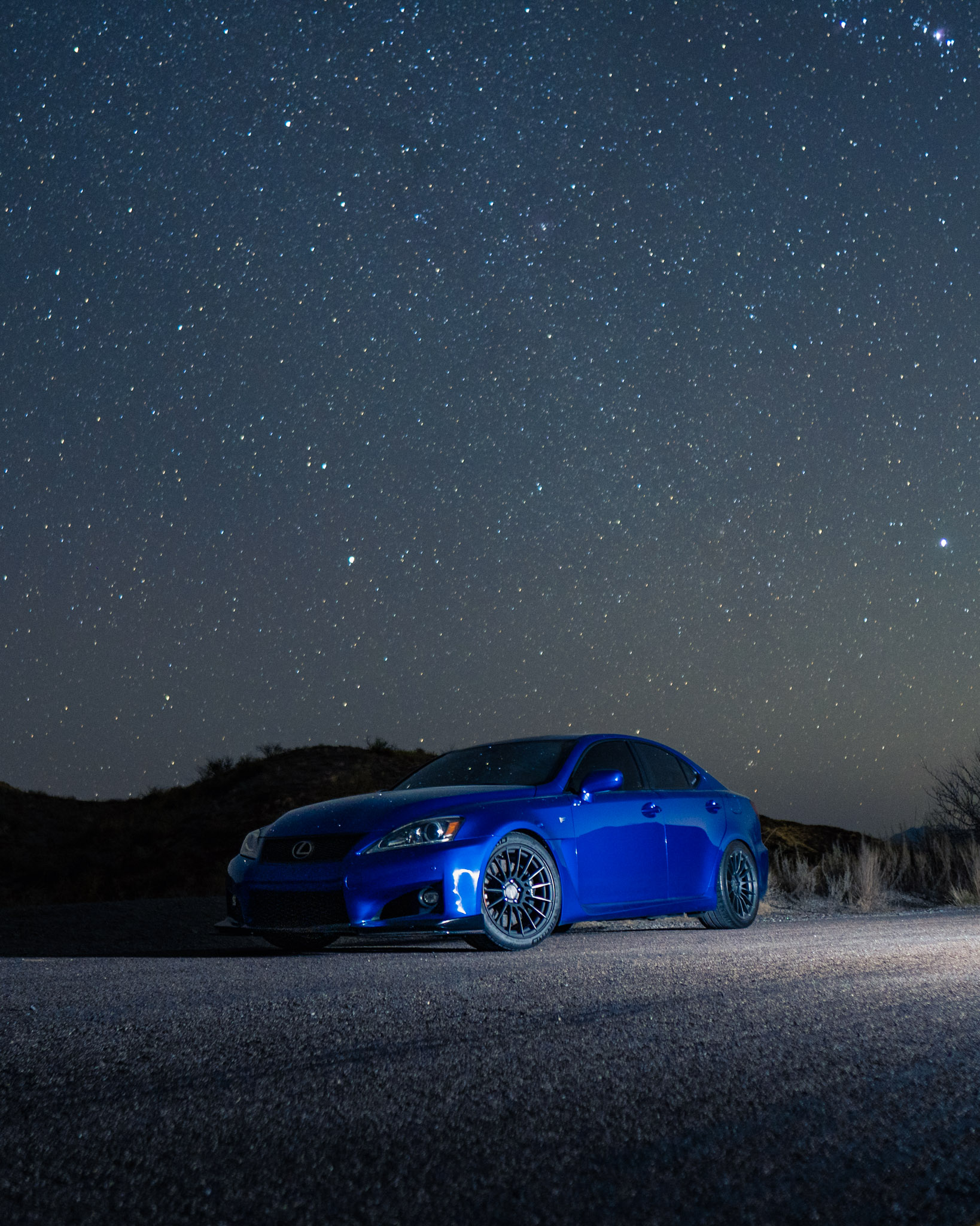 Blue Lexus IS-F illuminated under a star-filled desert night sky