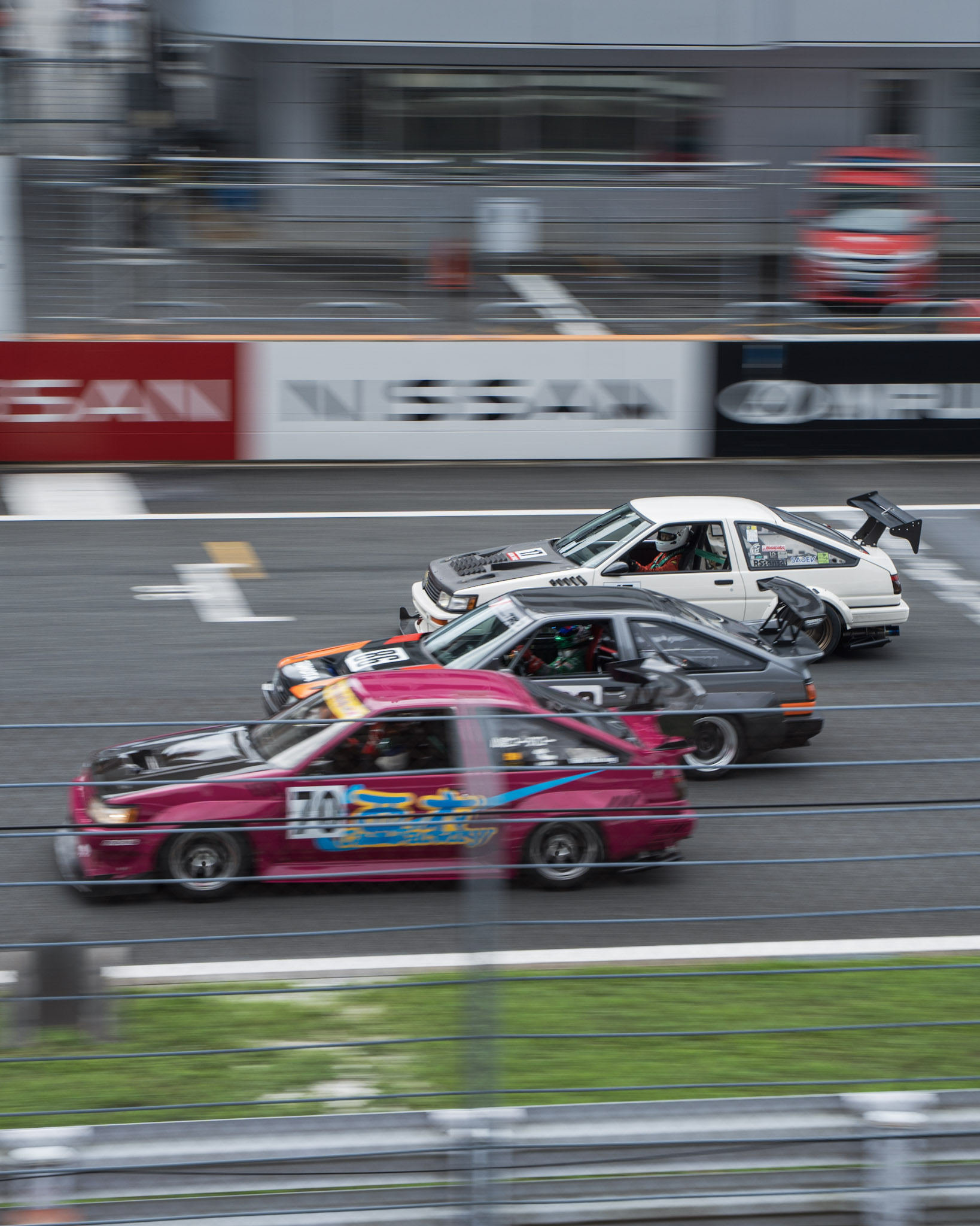 Three AE86-era drift cars racing three-wide past the main straight at Fuji Speedway